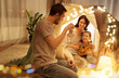 © Syda Productions - family, hygge and people concept - happy mother, father with lantern and little daughter with teddy bear playing in kids tent at night at home