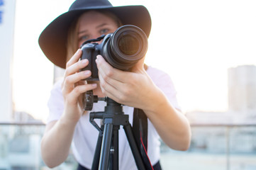 Canvas Print - girl photographer with a camera and a tripod on a background of the city, she photographs at sunset, a woman shoots a video