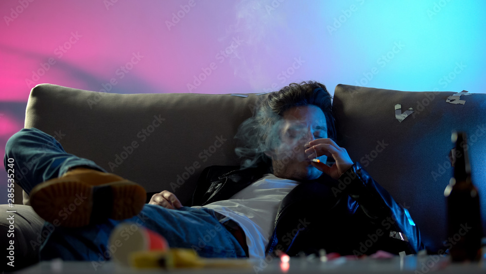 Careless drunk man smoking cigarette and relaxing on sofa at nightclub  party Stock Photo