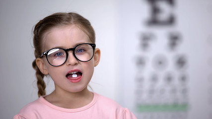 Wall Mural - Cute child girl in glasses taking pills for eyesight treatment, helpful vitamins