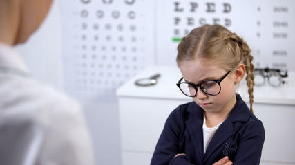 Wall Mural - Female doctor putting glasses on disgruntled girl, child feels insecure, upset