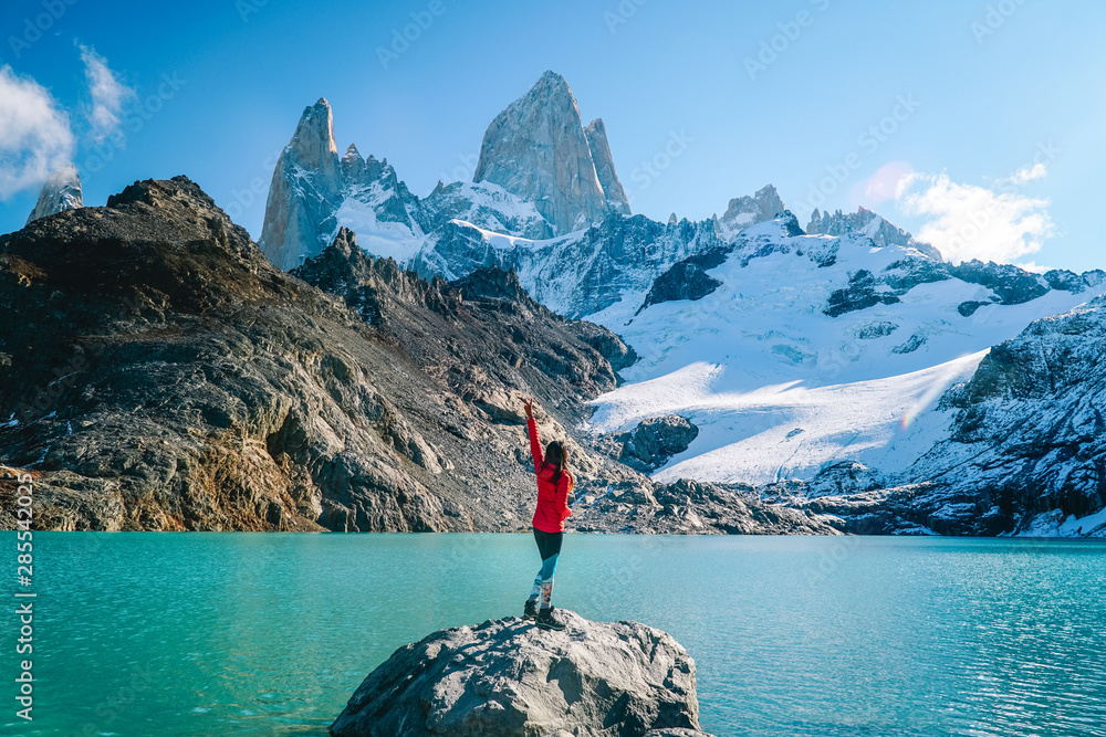 Tourist woman on Mount Fitzroy, Patagonia trek. Scenic view of snowcapped mountain tops. Blue sky, turquoise blue lake and scenic rock landscape. Shot in Argentina. Nature, travel, adventure, hiking. - obrazy, fototapety, plakaty 