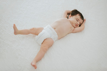 adorable baby girl sleeping in bed with arms and legs stretched - family and baby concept