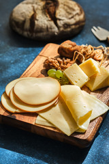 Wall Mural - Different varieties of cheese with grapes and walnuts on a wooden board.