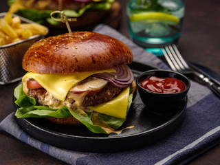 Big beef burger with onions and tomatoes. Juicy cheeseburger on a dark table