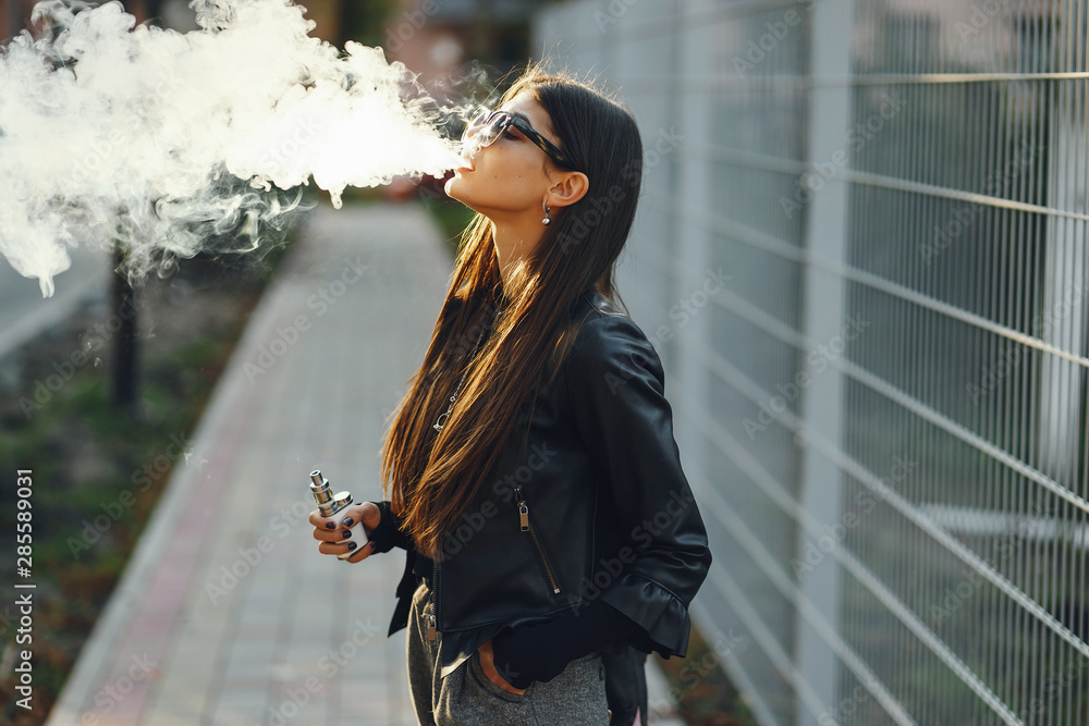 stylish girl smoking an e-cigarette as she is walking through the city  Stock Photo