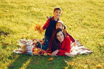 Wall Mural - Cute family in a autumn park. Happy mother with little kids. Family sitting on yellow leaves. Golden autumn.