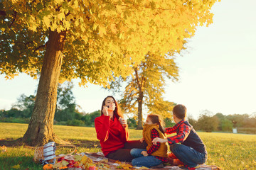 Wall Mural - Cute family in a autumn park. Happy mother with little kids. Family sitting on yellow leaves. Golden autumn.