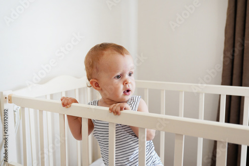 Cute Baby Standing In A White Round Bed White Nursery For