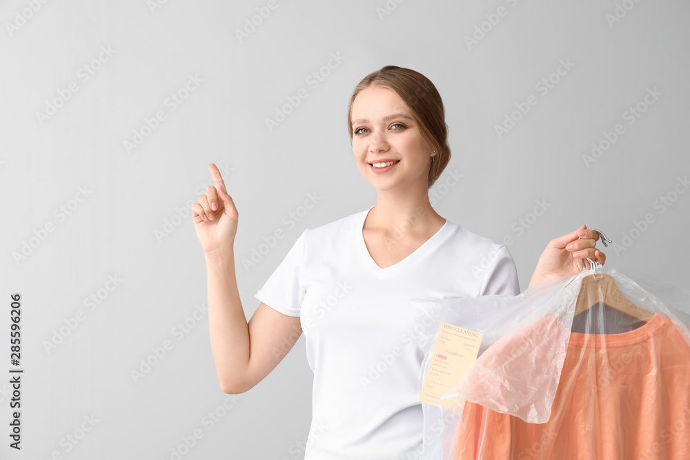 Woman with clothes after dry-cleaning pointing at something on light background