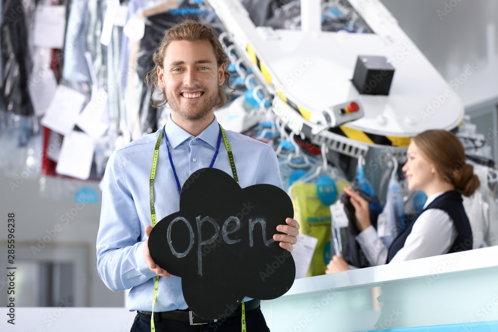 Worker of modern dry-cleaner's holding poster with text OPEN