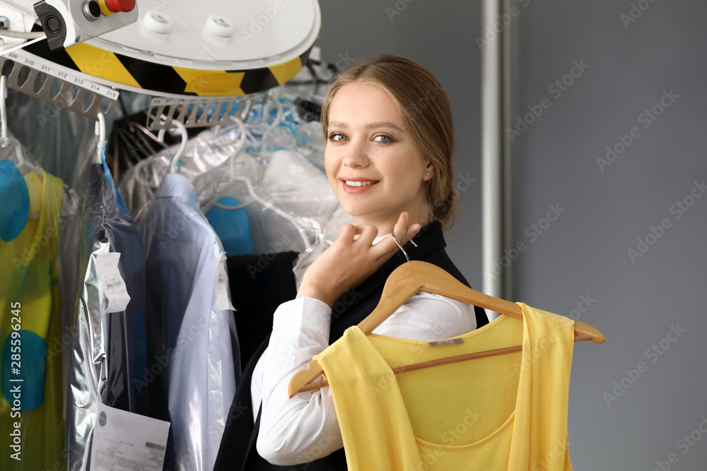 Worker of modern dry-cleaner's near rack with clothes