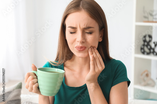 Fotografía Young woman with sensitive teeth and cup of hot coffee at home