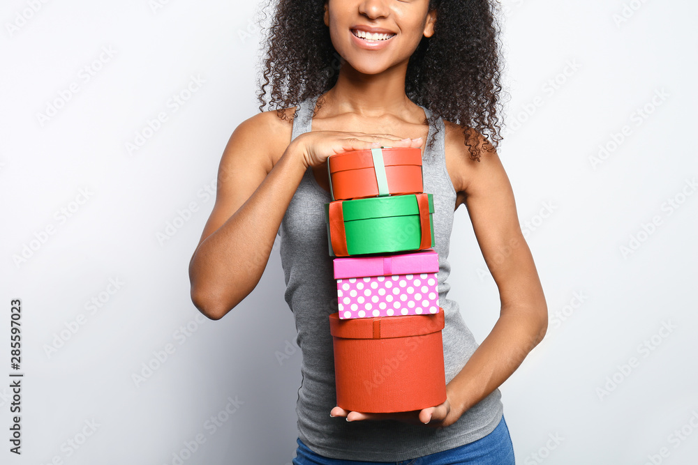 Beautiful African-American woman with gift boxes on white background