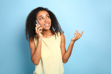 Wall Mural - Portrait of beautiful African-American woman talking by mobile phone on color background