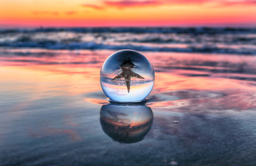 Wall Mural - Beautiful sunset on the beach in Slowinski National Park near Leba, Poland. View through a glass, crystal ball (lensball) for refraction photography. Wild, untouched nature.
