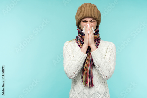 Fotografía Health and medicine concept - Young woman blowing nose into tissue, on a blue background