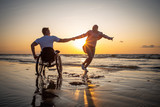 Fototapeta Na sufit - Handicapped man in wheelchair and his girlfriend on a beach at sunset