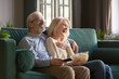 © fizkes - Cheerful old couple holding remote control laughing watching funny tv