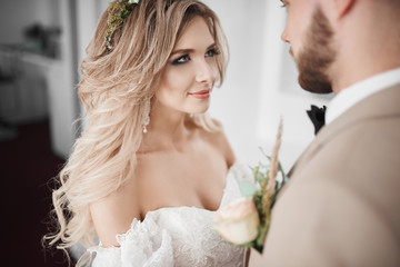 Wedding photo session at the hotel. Tender and bright photos. Sensual bride and stylish groom are standing by the bright window.