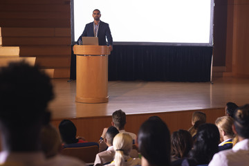 businessman standing around the podium and giving speech in front of audience in the auditorium