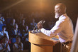 © WavebreakMediaMicro - Businessman standing near podium and giving speech to the audience in the auditorium