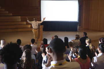  Businessman standing and giving presentation in auditorium 