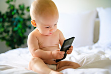 A Portrait Of A Cute Baby Checking Smartphone Lying In A Bed