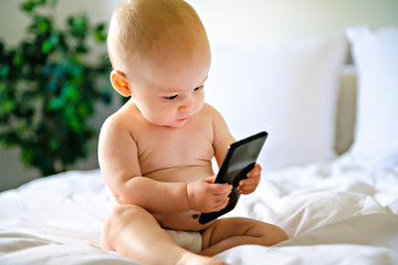 A portrait of a cute baby checking smartphone lying in a bed