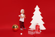 © oes - Happy little girl child in Santa hat standing next to a wooden white christmas tree. Nearby are gift boxes. Isolated on red background. Space for Your Text. Sale, holidays, christmas, new year concept