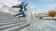 © Gorodenkoff - Cheerful and Happy Businessman in a Suit is Holding Coffee and Jumping While Walking Down the Stairs. Scene Shot in an Urban Concrete Park Next to Business Center. Sunny.