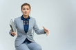 Studio photo a waist-high portrait of a cute young woman girl in a business suit on a white background with a folder in hands. Sits in a chair right in front of the camera, explains, with emotions.