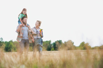 Young Caucasian family walking across field with young child on her fathers shoulders with the wife holding a bouquet of flowers