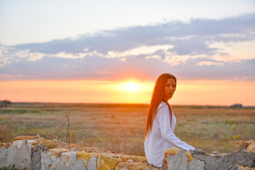 Canvas Print - girl in white clothes at sunset on the ruined wall