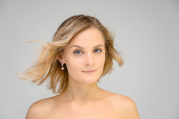 Closeup photo studio portrait of a fashionable pretty blonde young woman girl with beautiful hair on a white background. Standing right in front of the camera. Beauty, cosmetics.