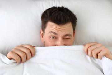 Poster - Handsome man covering his face with blanket while lying on pillow, top view. Bedtime