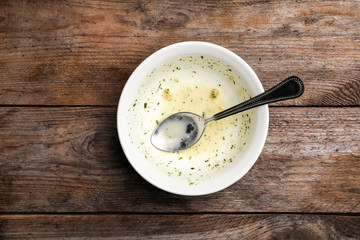 Dirty bowl with food leftovers and spoon on wooden background, top view