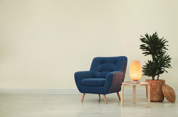 Poster - Stylish room interior with comfortable armchair and plant near beige wall. Space for text