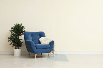 Poster - stylish room interior with comfortable armchair and plant near beige wall. space for text