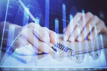 Forex graph on hand taking notes background. Concept of research. Double exposure