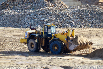 Wall Mural - Large heavy front-end loader or all-wheel bulldozer for mechanization of loading, digging and excavation operations in open quarry. Crusher plant with belt conveyor, crushing process, grinding stone