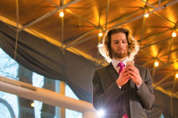 Wall Mural - Low angle view of confident young businessman text messaging on smart phone while standing against roof