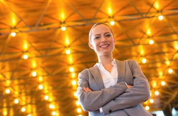 Wall Mural - Confident young businesswoman standing with arms crossed against illuminated roof