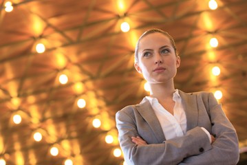 Wall Mural - Confident young businesswoman standing with arms crossed against illuminated roof