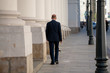 © spritnyuk - Back view of successful middle aged man in stylish dark business suit walking down city street with smartphone and bag in New York