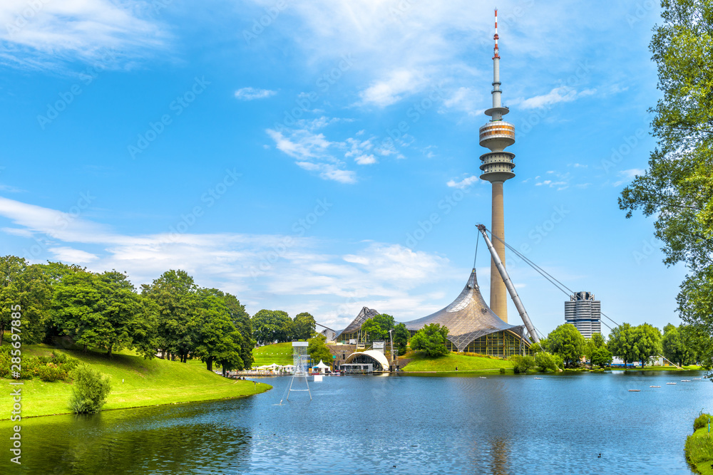 Munich Olympiapark in summer, Germany. It is Olympic Park, landmark of Munich. Scenic view of former sport district. Scenery of Munich with tower and lake. Beautiful landscape of Munich city. - obrazy, fototapety, plakaty 
