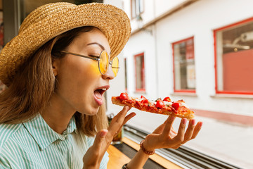 Wall Mural - Funny asian girl in hat eating focaccia sort of pizza