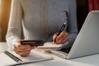 © NINENII - Female businessman use a laptop computer and take notes in the notebook at the office desk in the morning.
