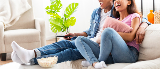 Wall Mural - Cheerful couple sitting on couch watching funny videos on tv