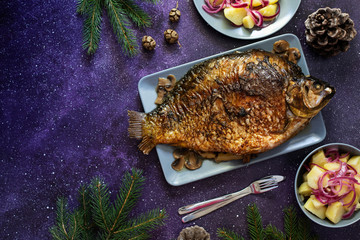 Christmas whole Carp baked with mushrooms. Served on a dark background with potato salad. Traditional Christmas Eve meal. Top view. Space for text